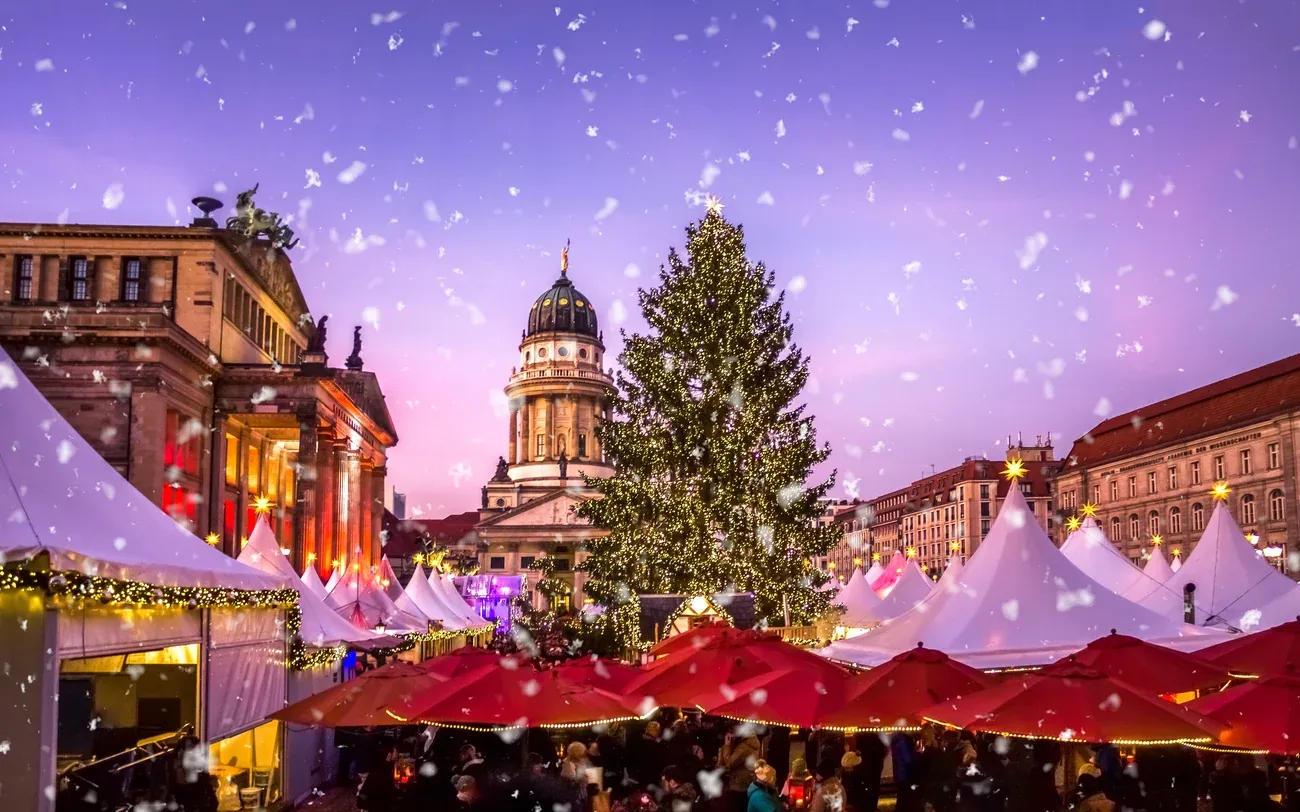 Red umbrellas, white tents and the Christmas tree of the WeihnachtsZauber on Gendarmenmarkt in Berlin, the French Cathedral behind