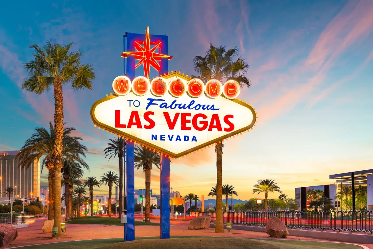 The neon Welcome to Fabulous Las Vegas Nevada sign framed by palm trees at sunset