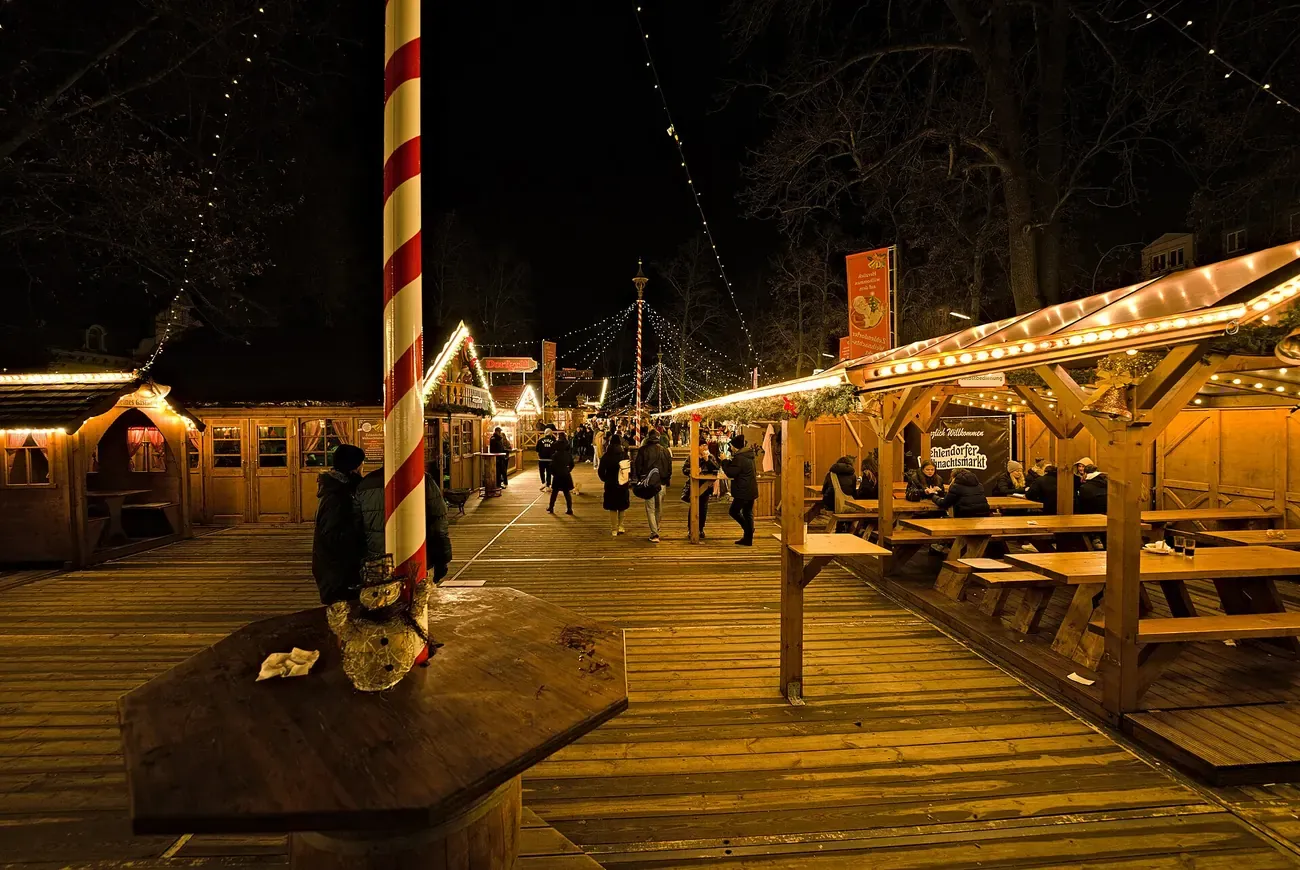Wooden huts and a striped pole at the Zehlendorf Christmas market at night, Berlin