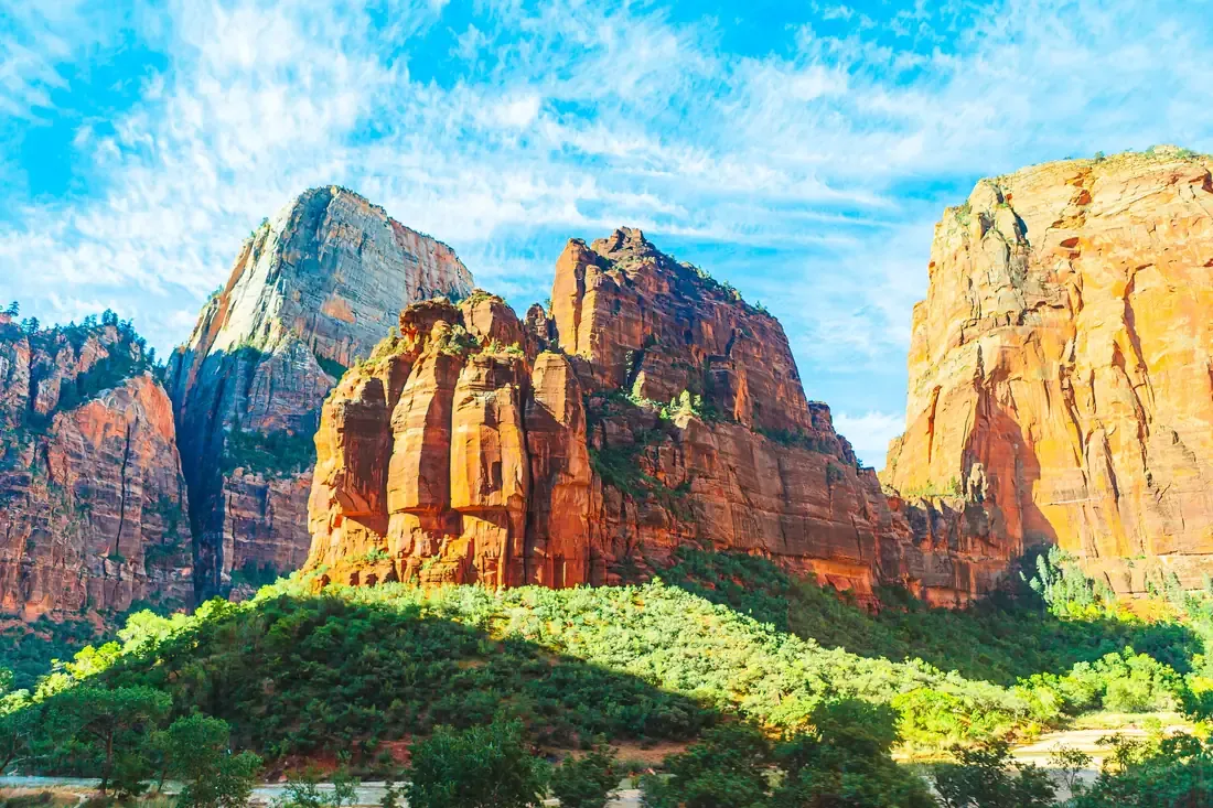 Sunlit red and white sandstone cliffs rising above the wooded floor of Zion Canyon in Zion National Park, Utah