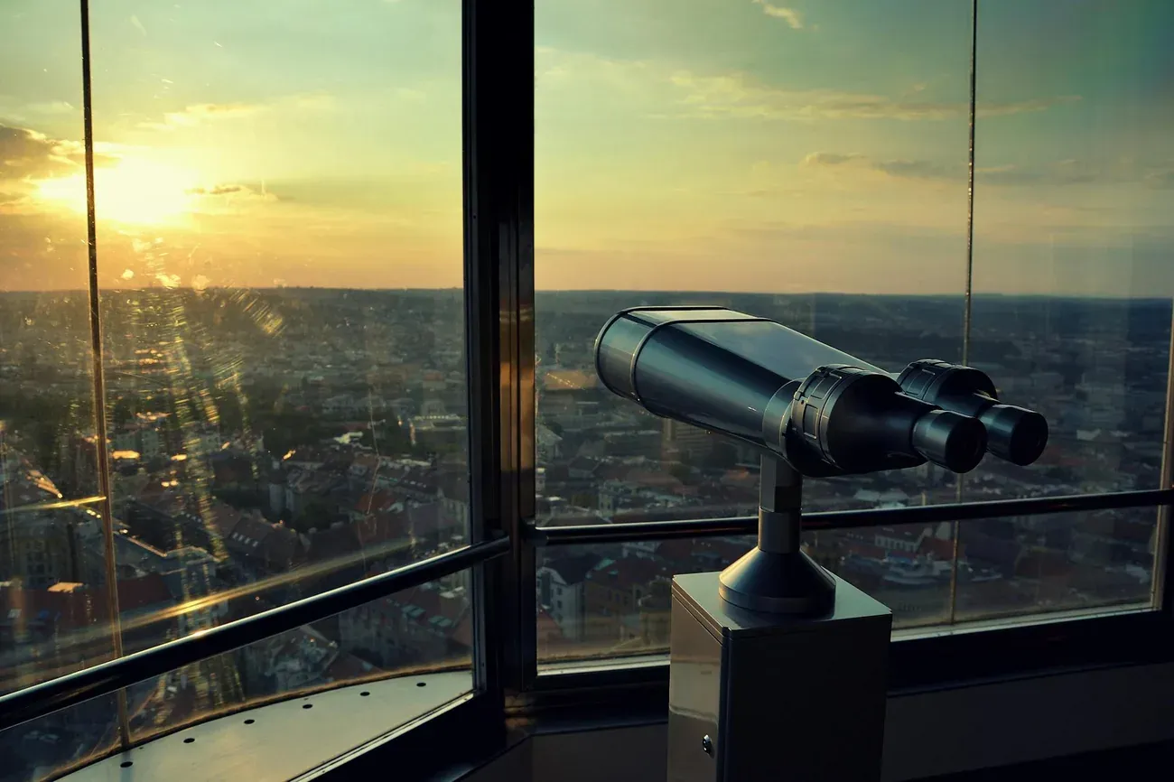 A viewing telescope at the observation deck window of the Zizkov Television Tower at sunset