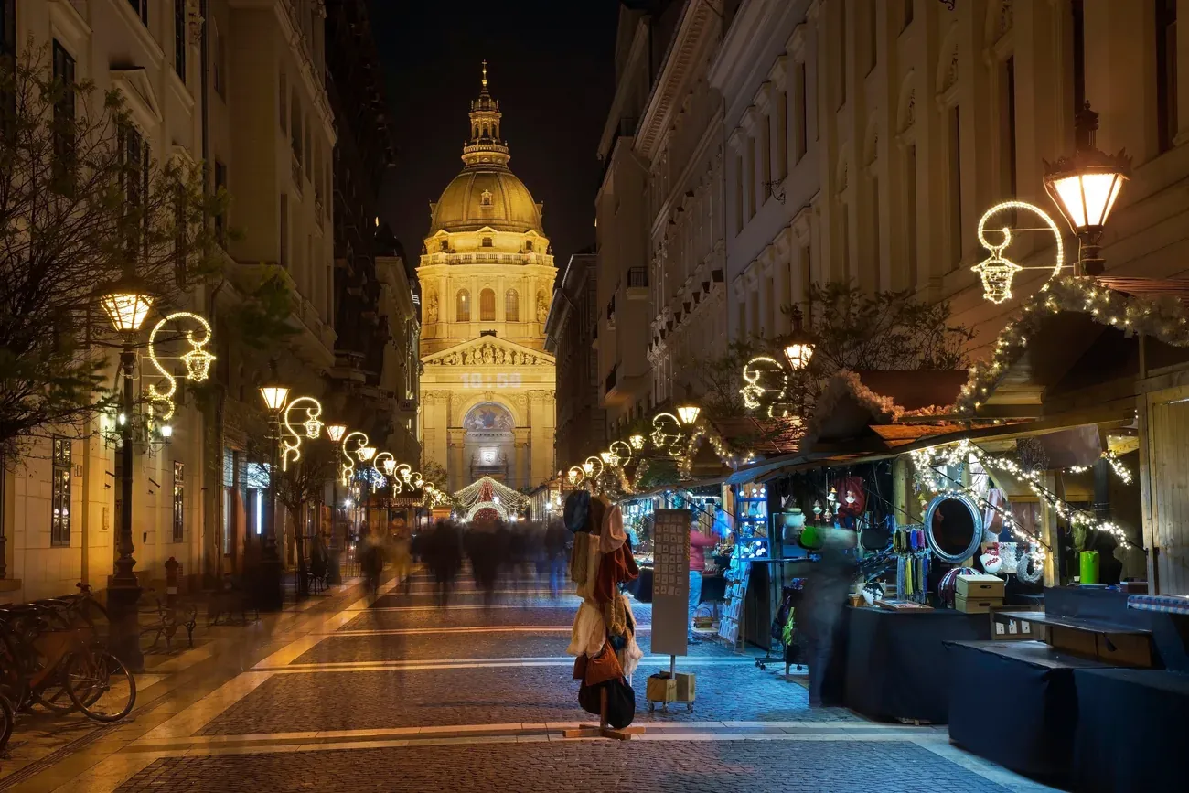 Christmas market stalls along Zrínyi utca in Budapest at night, with St Stephen's Basilica lit up at the end of the street